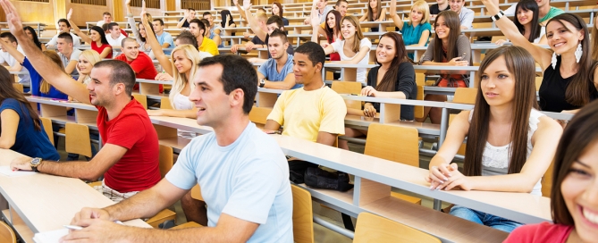 College students in lecture hall with raised hands