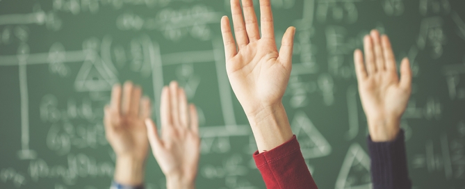 Students raised up hands green chalk board in classroom