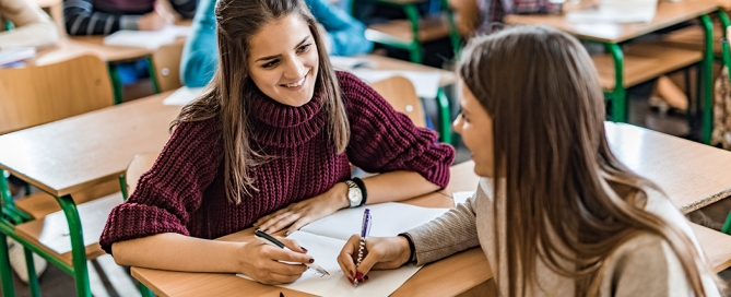 A smiling female student communicates with a friend during the lecture in the classroom