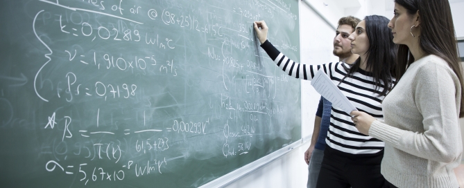 Three students work on a math problem at the blackboard