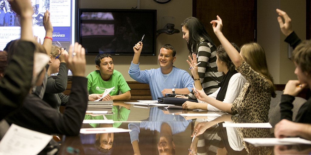 Students sitting at a conference table, raising hands.