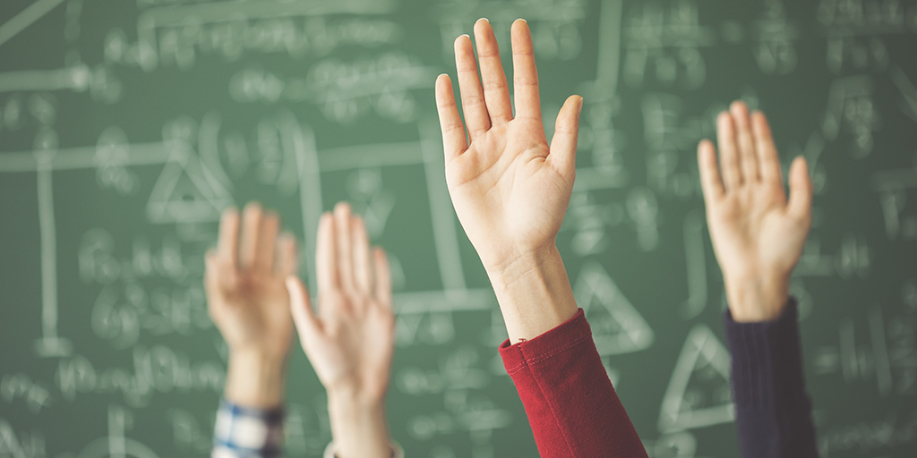 Students raised up hands green chalk board in classroom