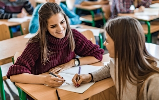 A smiling female student communicates with a friend during the lecture in the classroom