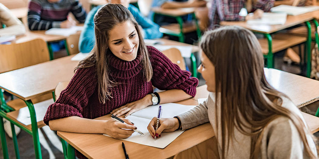 A smiling female student communicates with a friend during the lecture in the classroom