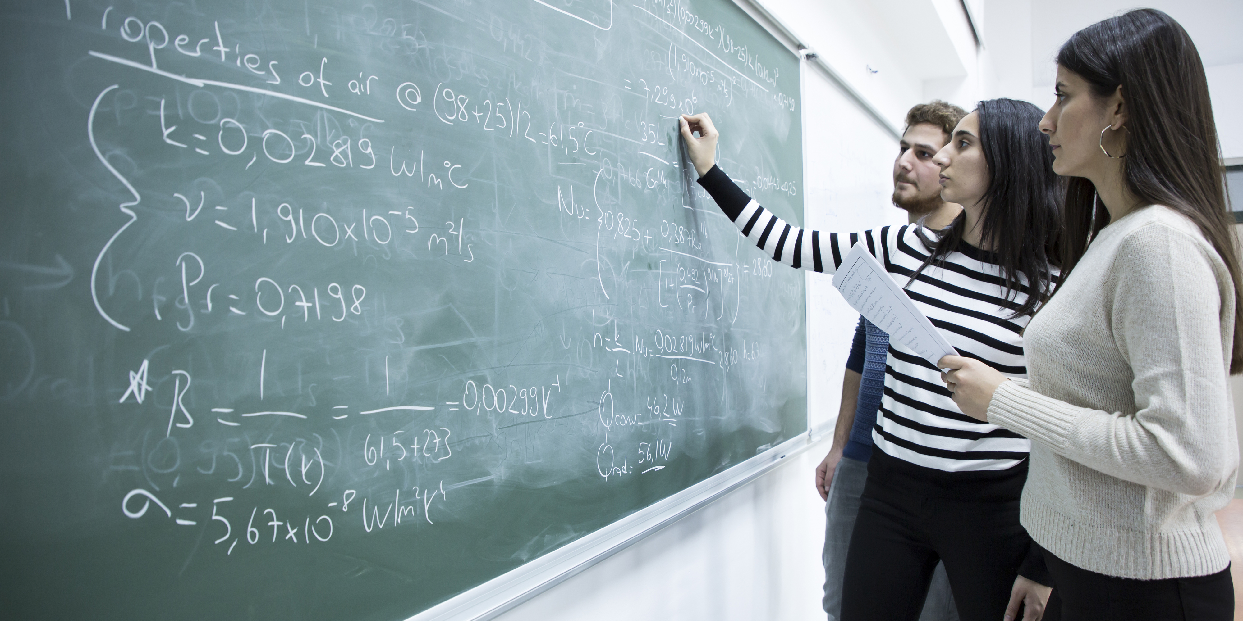 Three students work on a math problem at the blackboard