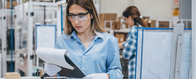 A factory employee in safety goggles examines a clipboard