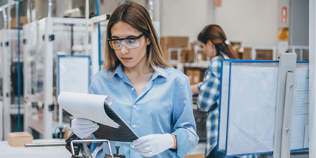 A factory employee in safety goggles examines a clipboard