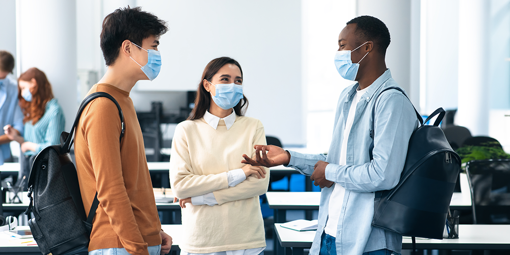 Three students in masks talk after class